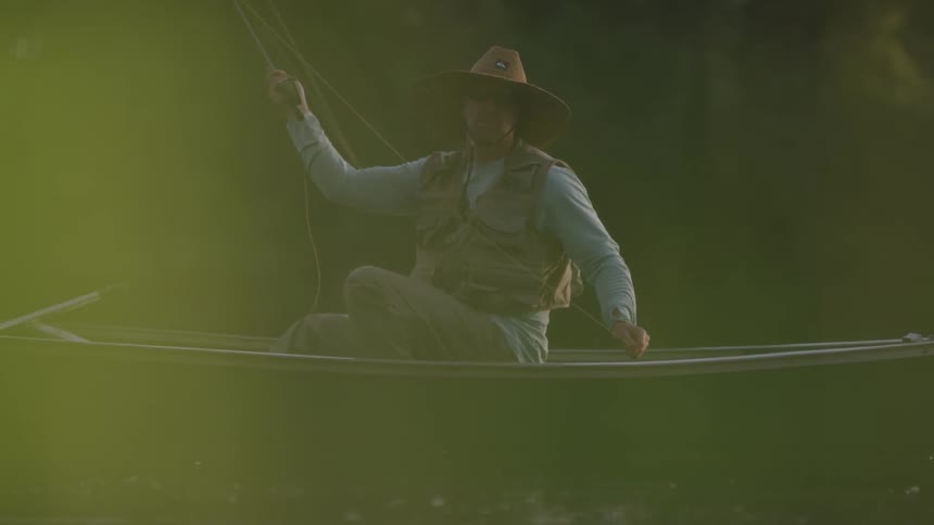 A man with cowboy hat fishing on a boat at the river