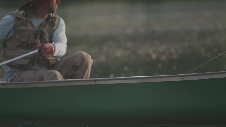 A man sits in a small boat with a fishing pole