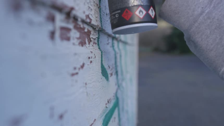 A persons hand as they spray paint green paint onto a wall