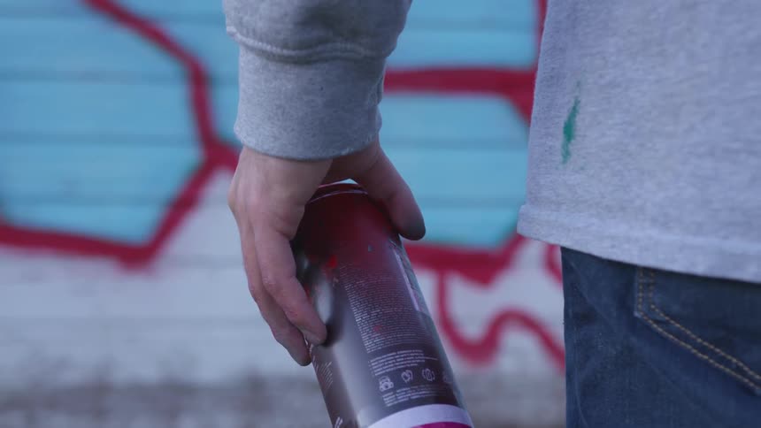 A person standing before a wall covered in graffiti holding a can of spray paint