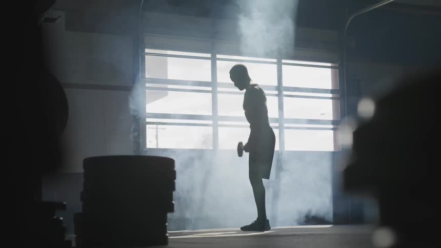 A man stands in a gym as he does curls with dumb bells