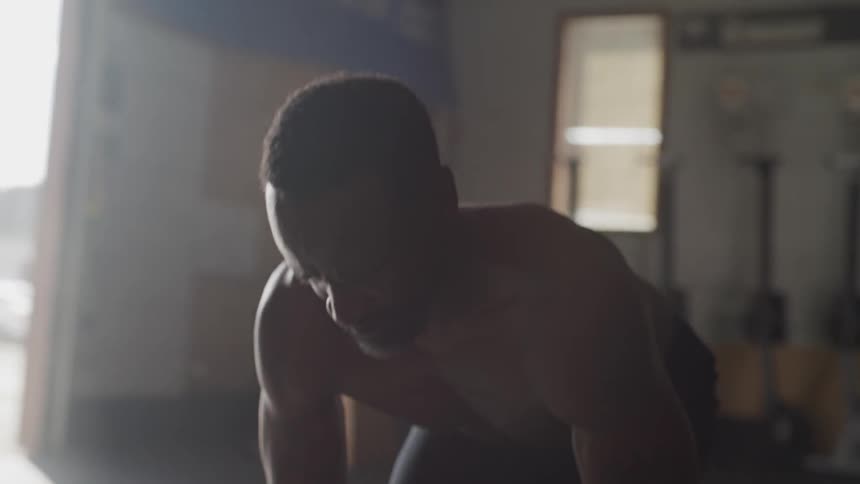 A shirtless man lifts weights in a gym