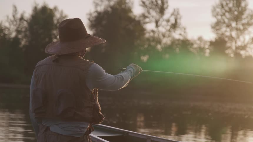 Man wearing a hat holds a fishing rod as he fishes in a lake