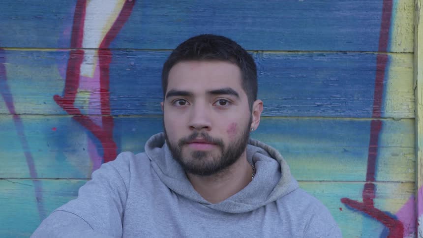 A man sits in front of a graffiti painted wall