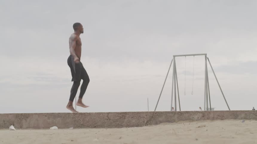 A shirtless muscle man jumps rope on a beach