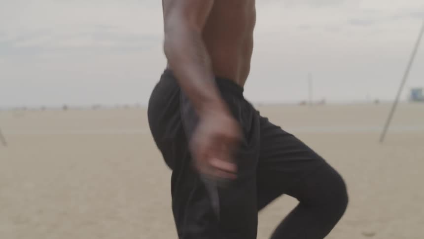 Shirtless muscular black man jumps rope on the white sand beach during daylight