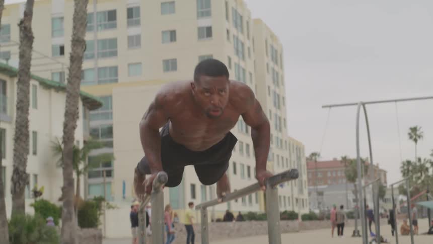 Muscular black man does triceps dips on parallel bars at public park on a cloudy day