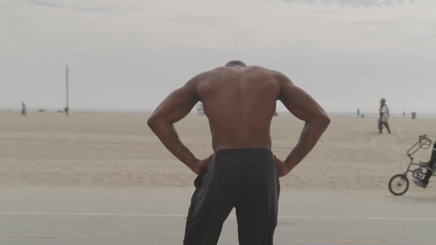 Half naked man in a sport shorts is warming up on a beach