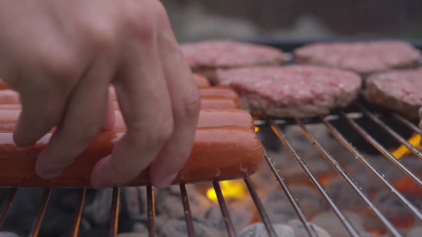 A person places a hot dog on a hot grill
