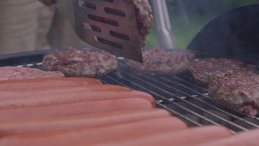 A man flips a burger on a charcoal grill