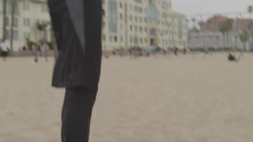 A very muscled man stretches and lifts weights on a sandy beach