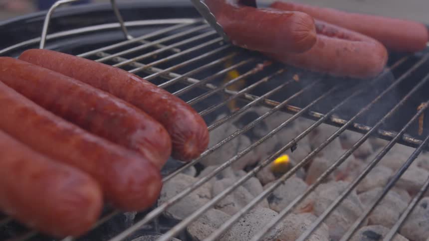 Person turns sausage on grill over coal