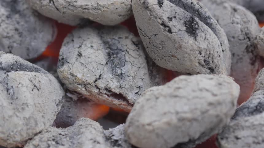 Light glows from within a pile of lit charcoal briquettes