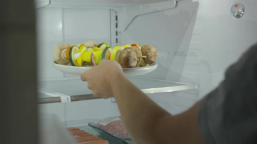 A person removing a pair of skewers from a refrigerator