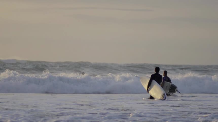 People walking along a scenic beach with waves and shoreline under a clear sky.