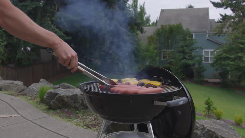A person flips over a hot dog cooking on a grill