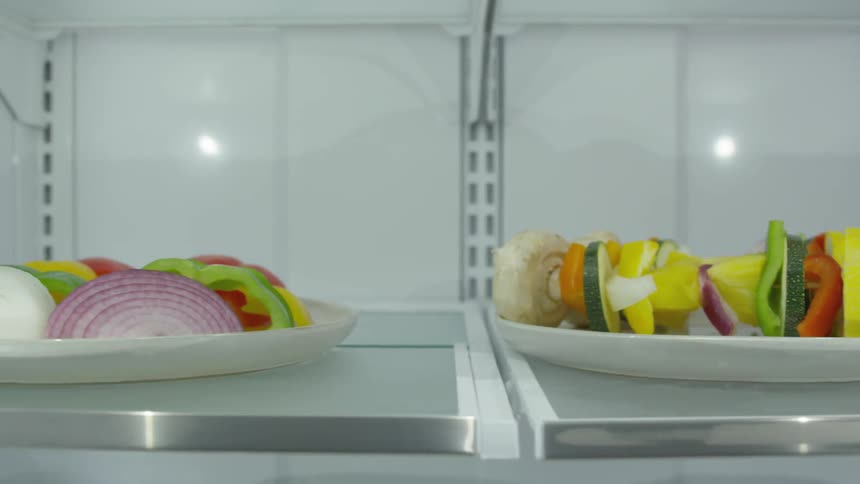 Vegetable kebabs and sliced veggies sit on plates on a shelf
