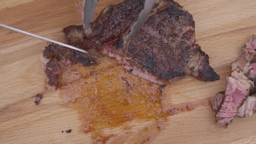 A steak being cut on a wooden cutting board
