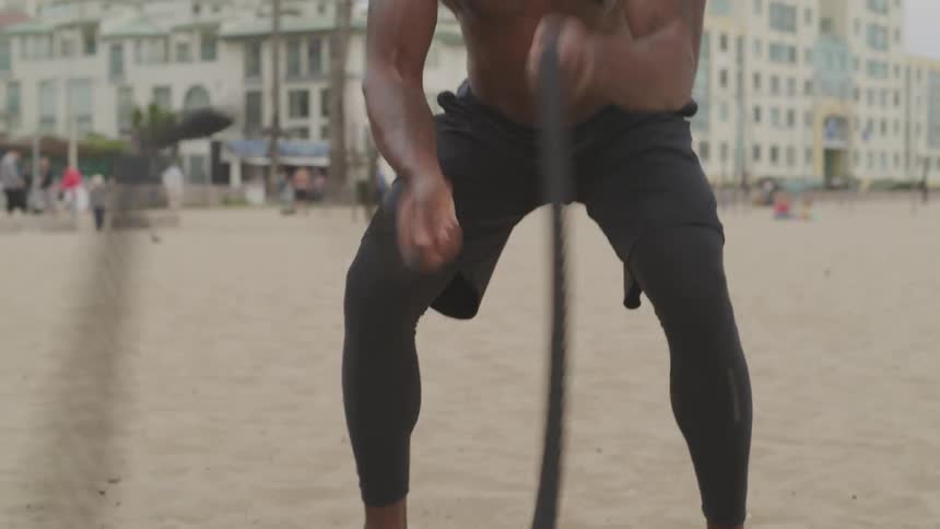 A man shakes large heavy ropes quickly on the beach