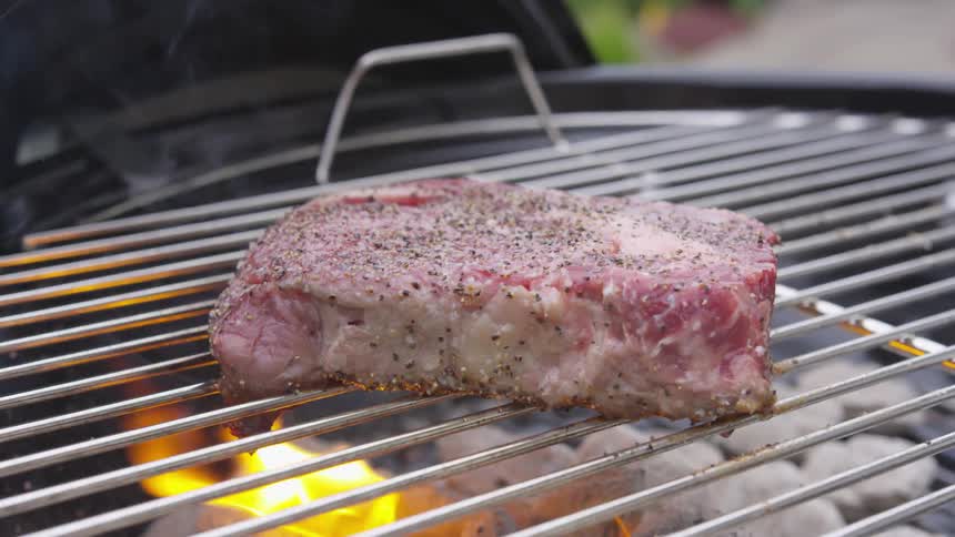 A steak cooks outside on a charcoal grill