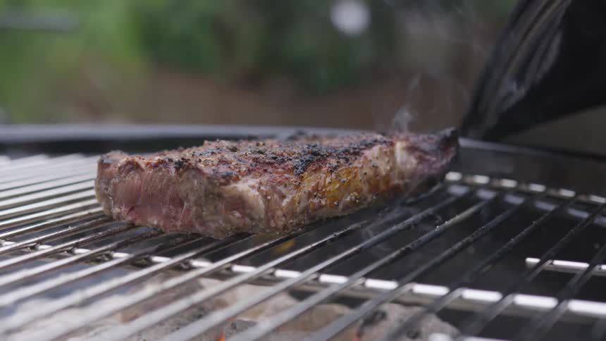 A steak is cooked on an outdoor charcoal grill