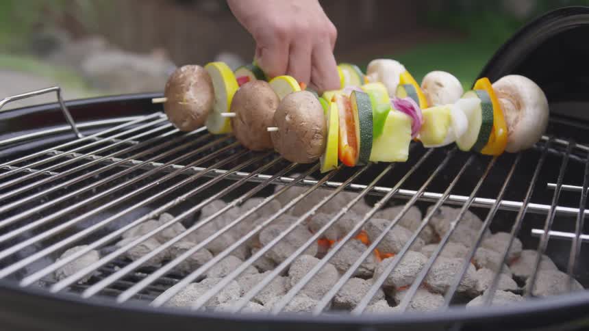 A man places vegetable kebab skewers on a hot charcoal grill