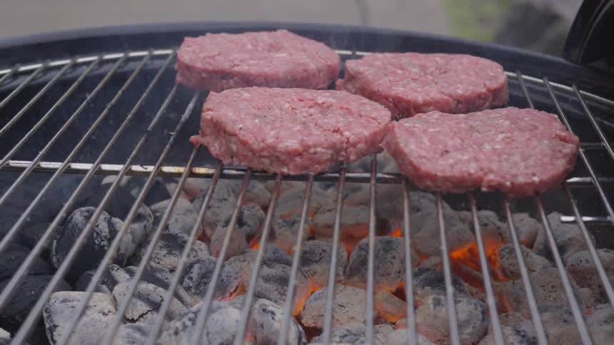 A person lays down a beef patty to a charcoal grill