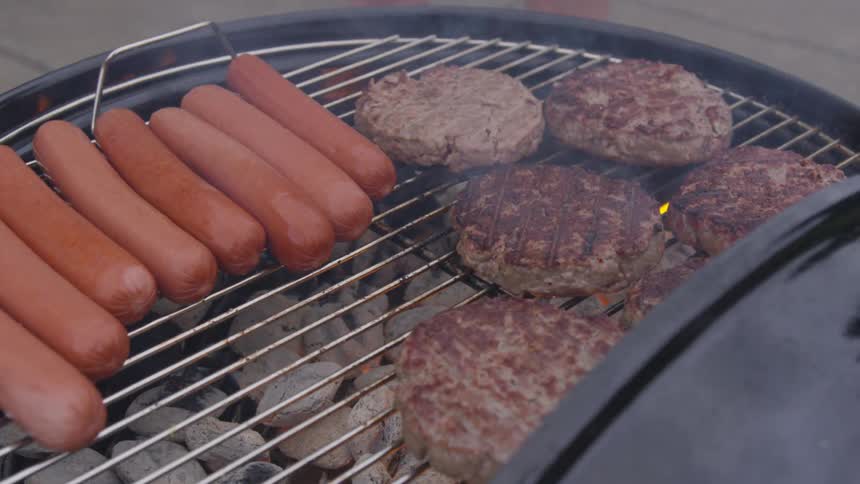 Five hamburgers and eight hot dogs cook on a charcoal grill
