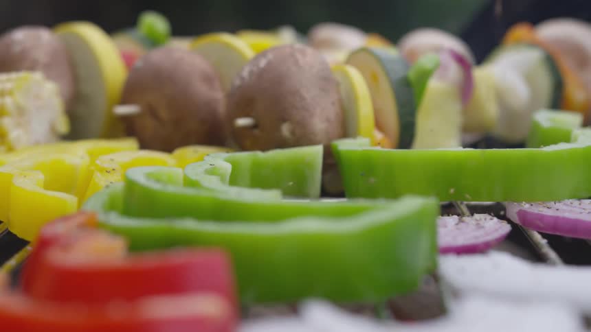Pepper is being sprinkled over onions bell peppers and other vegetables that are being cooked on a grill