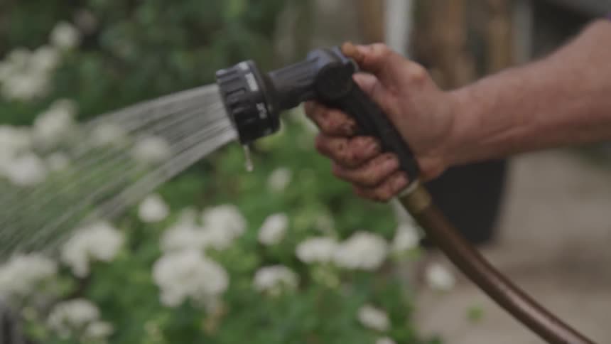 A man with mud all over his hand waters flowers with a garden hose