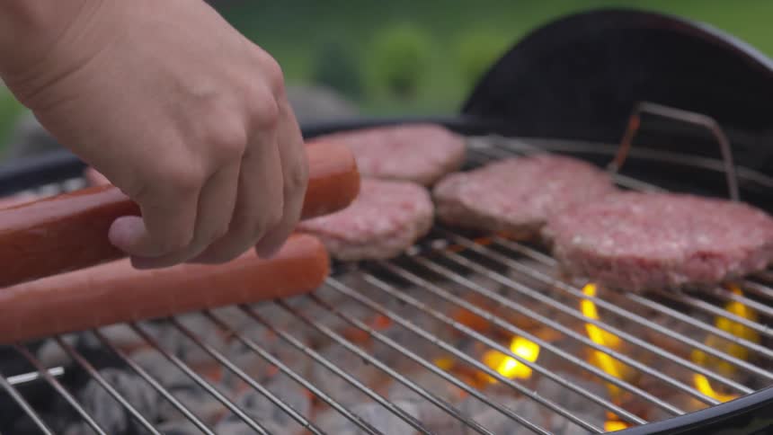 A person grilling hot dogs and hamburgers on a charcoal grill