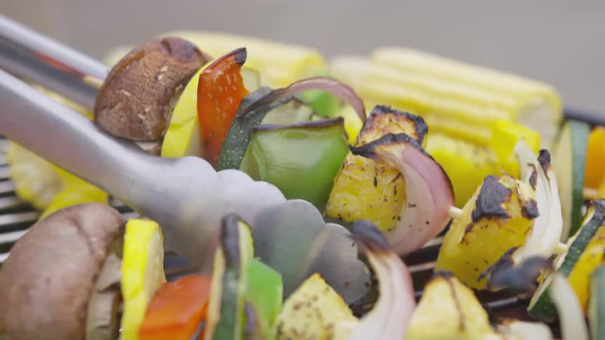 Tongs flip over a kabob of vegetables on an outdoor grill