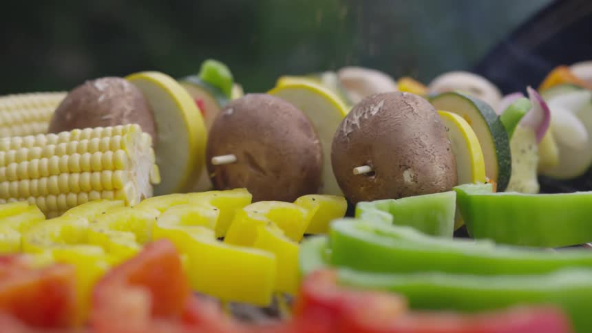 Vegetarian kebabs and other vegetables are salted near smoking grill