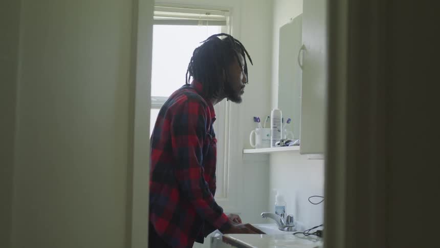A man is standing by the sink in his bathroom