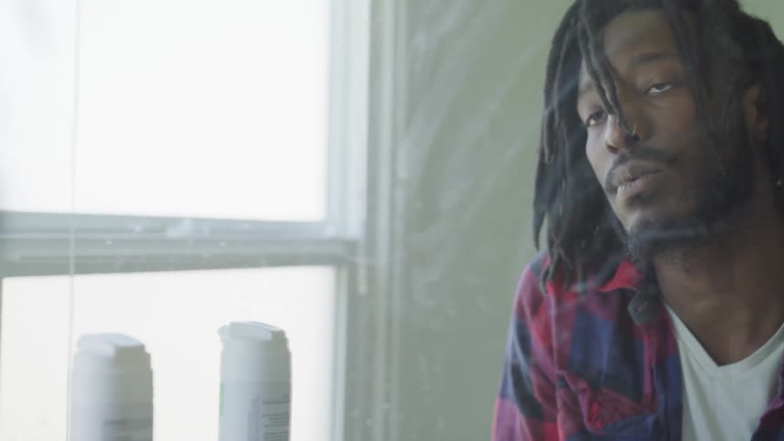 A man with dreadlocks looks up and at a mirror