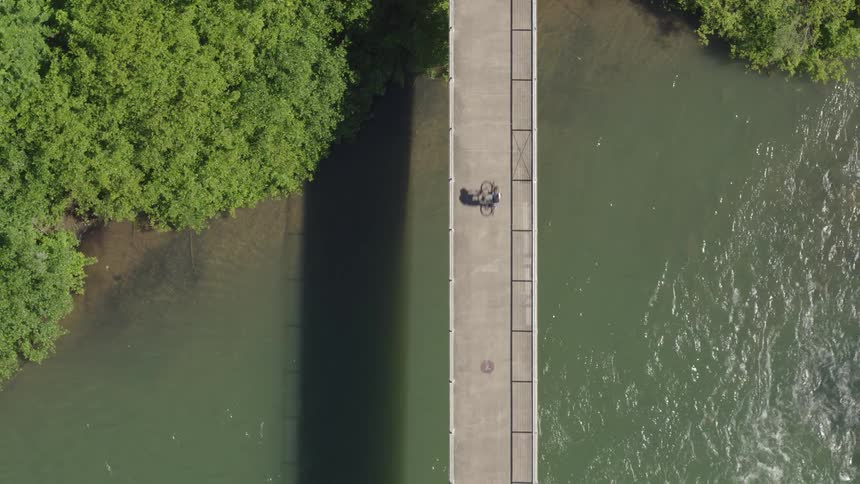 An aerial view of a bicyclist riding over a river bridge