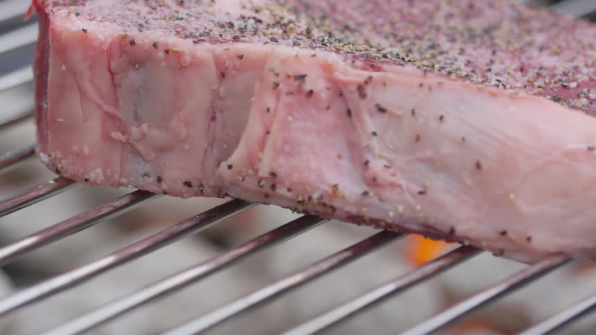 A seasoned steak is put on the grill outside