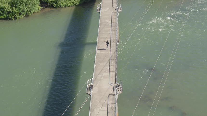 Someone is running on a bridge over a river and passes a cyclist going the other way