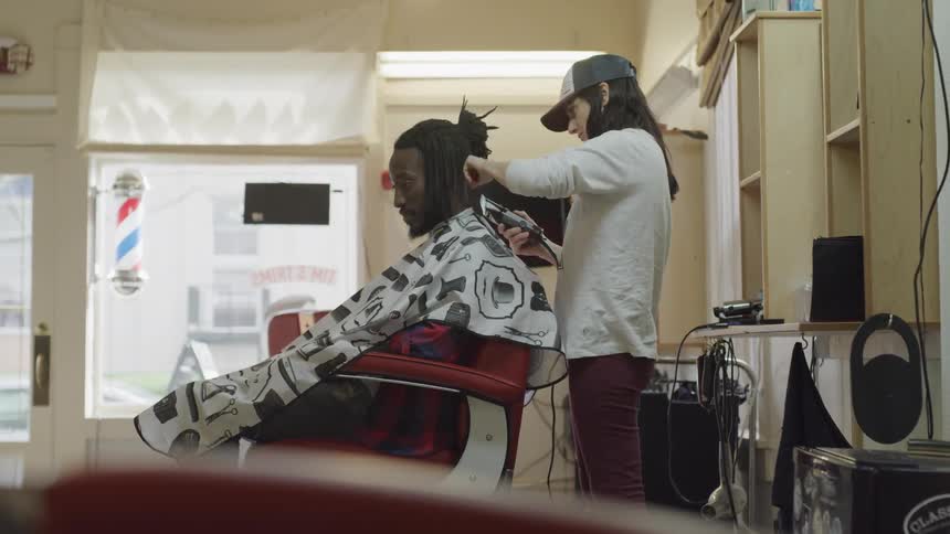 A woman uses a razor to trim a mans hair