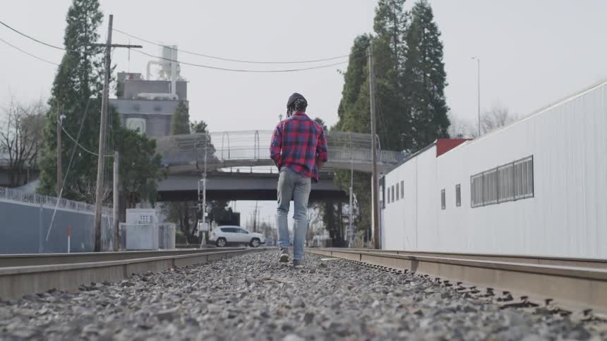 A man in a plaid shirt walks on railroad tracks in town