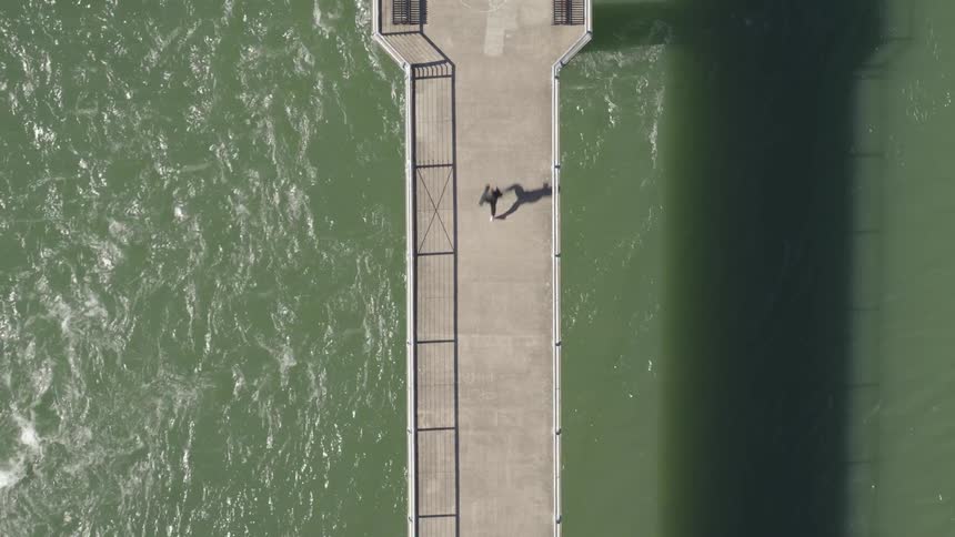 A person runs across a pedestrian bridge over water on a sunny day