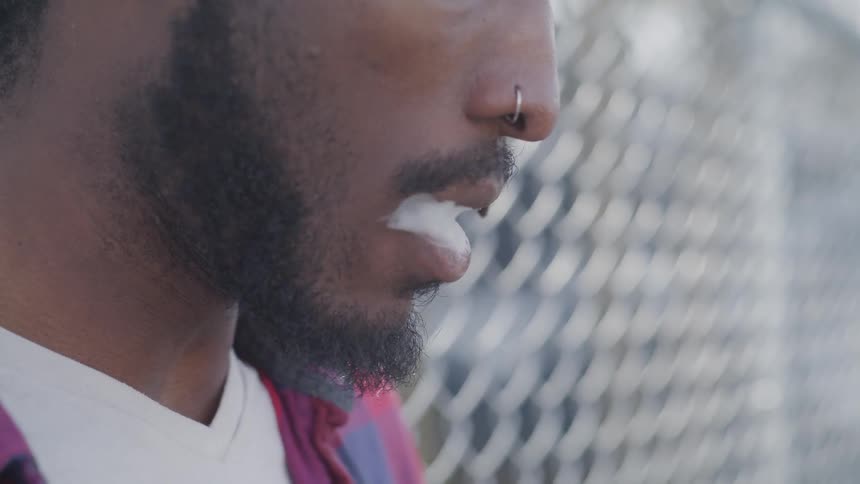 Man lifts cigarette to mouth and takes a puff