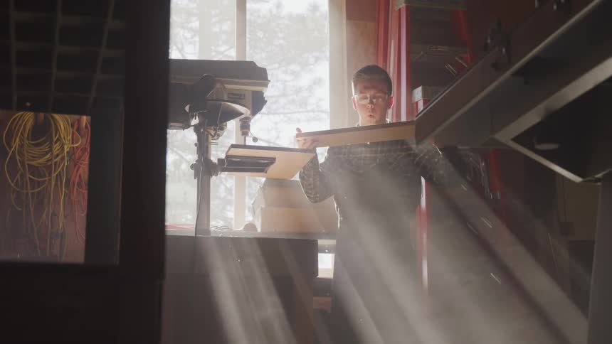 A man removing a wooden board from a drill press