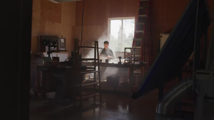 A carpenter works under a splash of light at his wood working shop