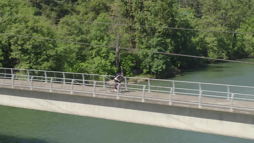 A person rides a bike across a pedestrian bridge over a river