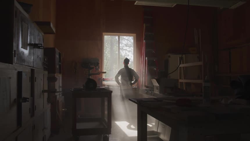 A man stands in a woodworking shop looking out a window