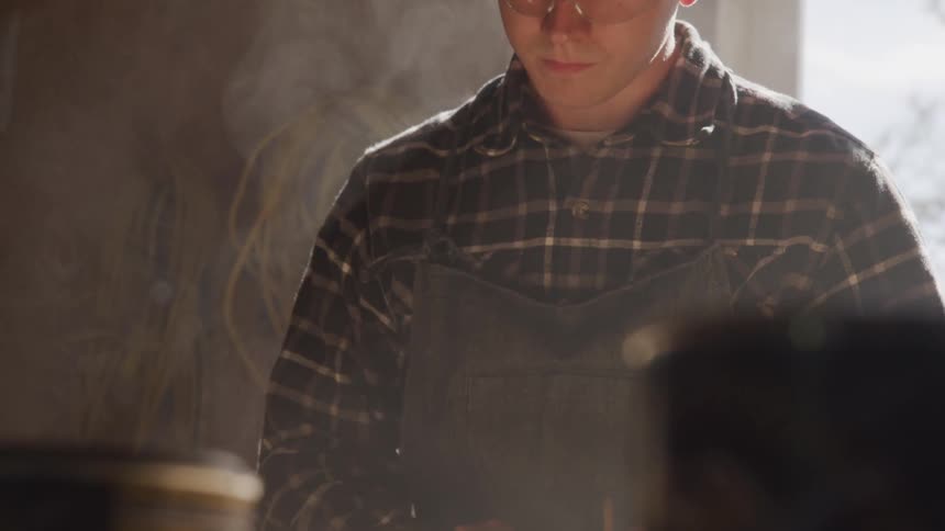 A man wearing goggles and an apron uses a pencil in his workshop