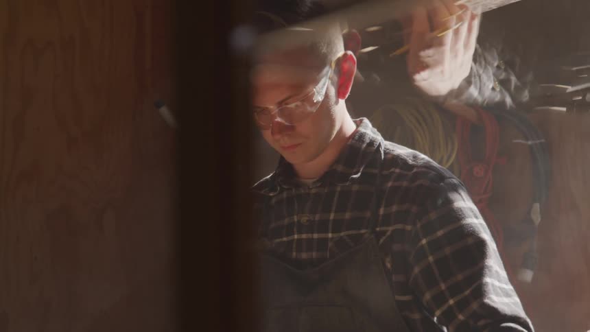 A man in a workshop measuring a wooden block with a measuring tape