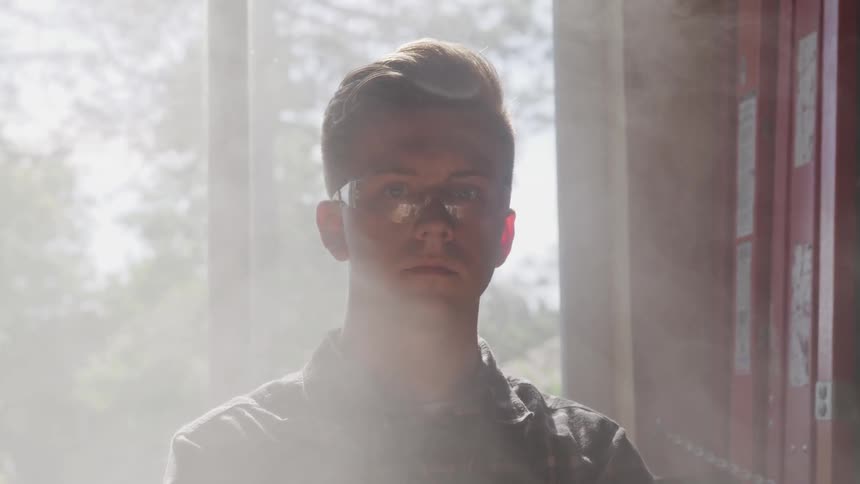 Blonde man wearing goggles looks at the camera while the sun streams through the window