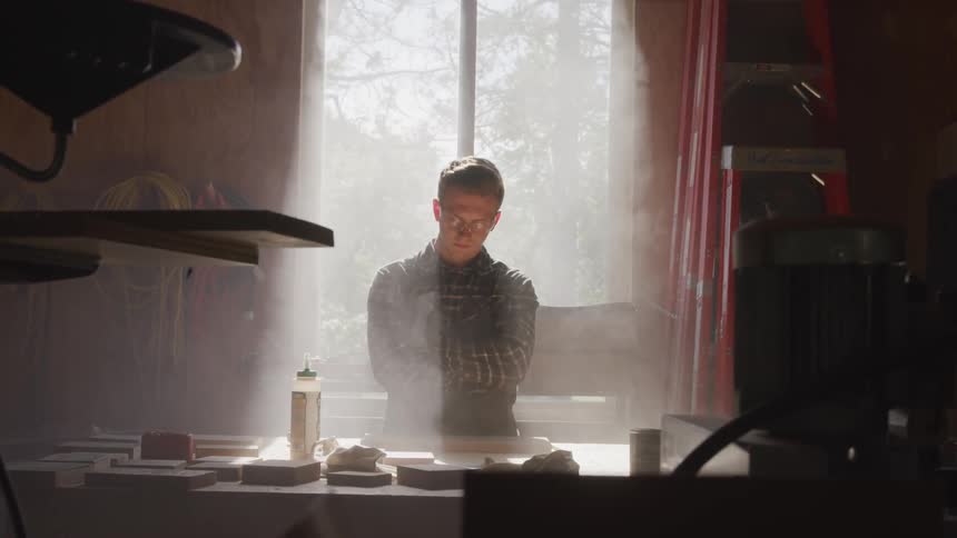 A man stands in front of a sunny window in a workshop